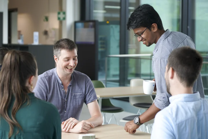 Colleagues gathered around table during informal discussion in modern office break area